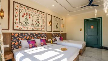 Habitación de hotel con dos camas, cabeceros estampados, obras de arte colgadas en la pared y un ventilador de techo.