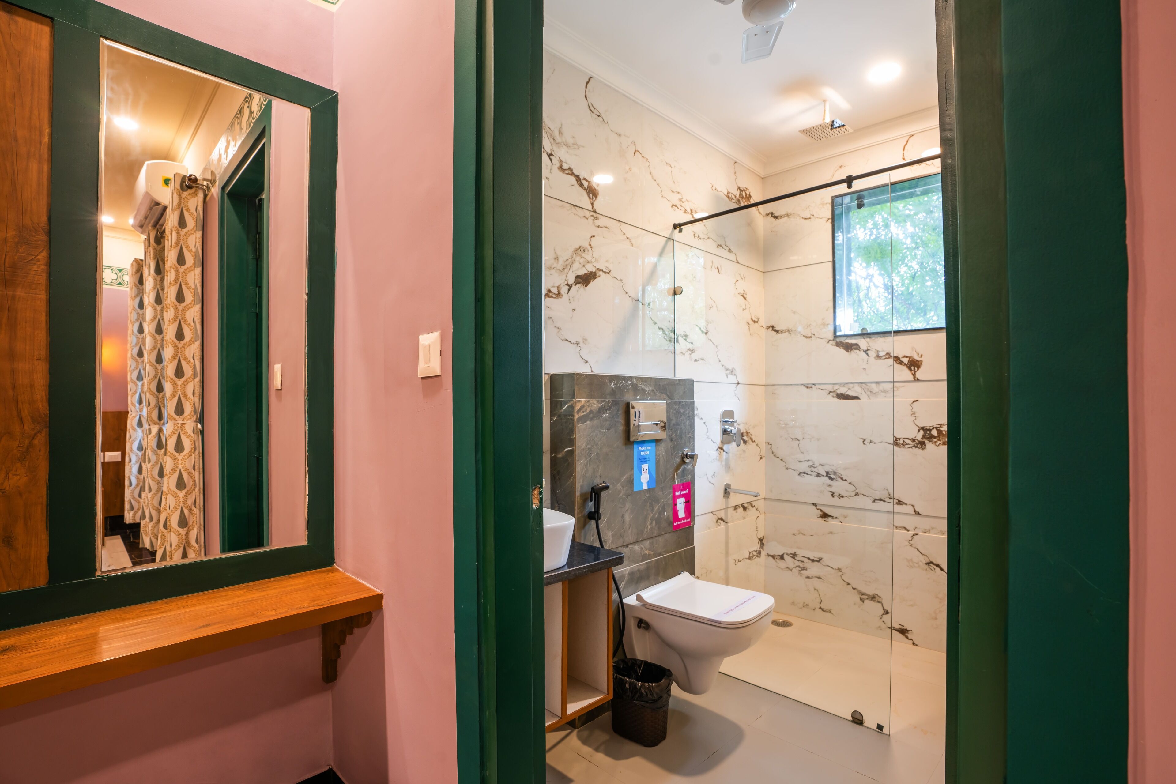 Un baño moderno con pared de ducha de mármol, lavamanos con encimera negra y espejo con marco de madera.