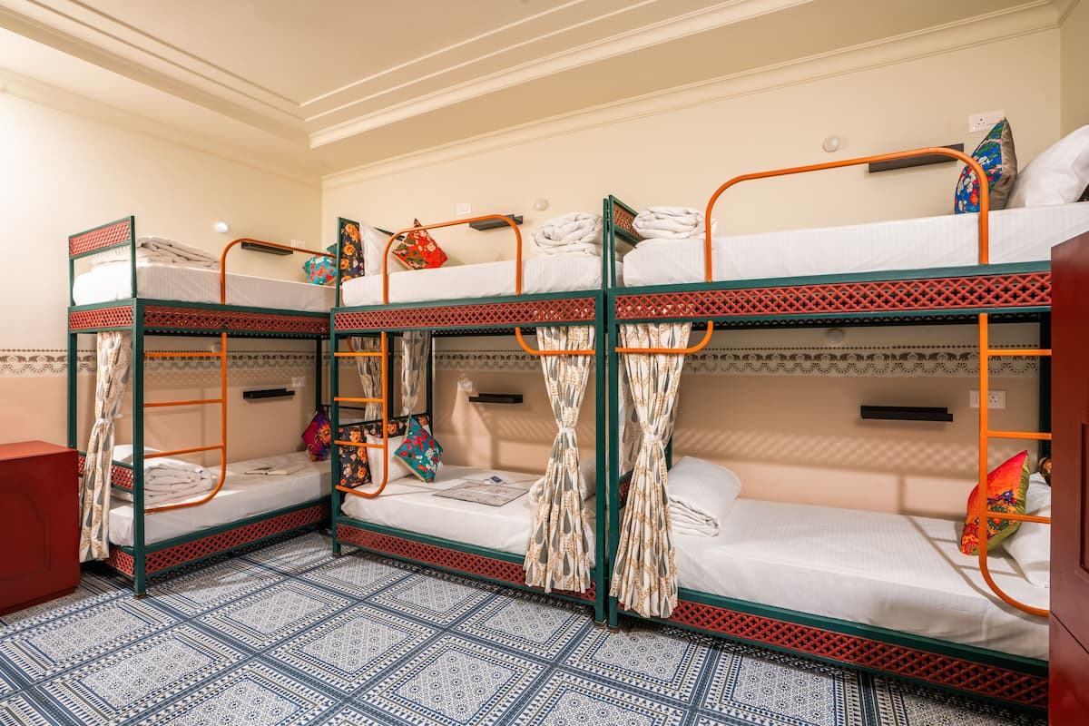 A dormitory room with bunk beds, a small shelf, and patterned floor tiles.