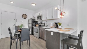 A modern kitchen with white cabinets, stainless steel appliances, and a central island with bar stools. - Modern luxe apt Airport+ NYC (Elizabeth)