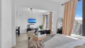 A modern hotel room with a large bed, a desk, a television, and a view of the city. - Modern luxe apt Airport+ NYC (Elizabeth)