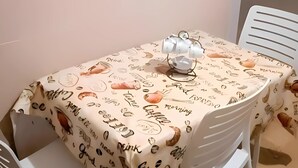 Un comedor con una mesa cubierta por un mantel con ilustraciones y texto relacionados con el café, rodeado de sillas blancas.