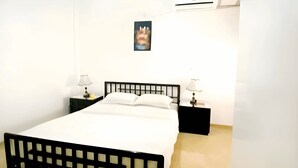 Un dormitorio con cama, dos mesitas de noche, un equipo de aire acondicionado y un cuadro en la pared.