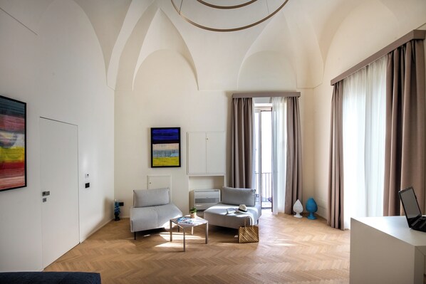 A modern living room with a sofa, armchair, and coffee table, a flat-screen TV, and a large window with curtains.