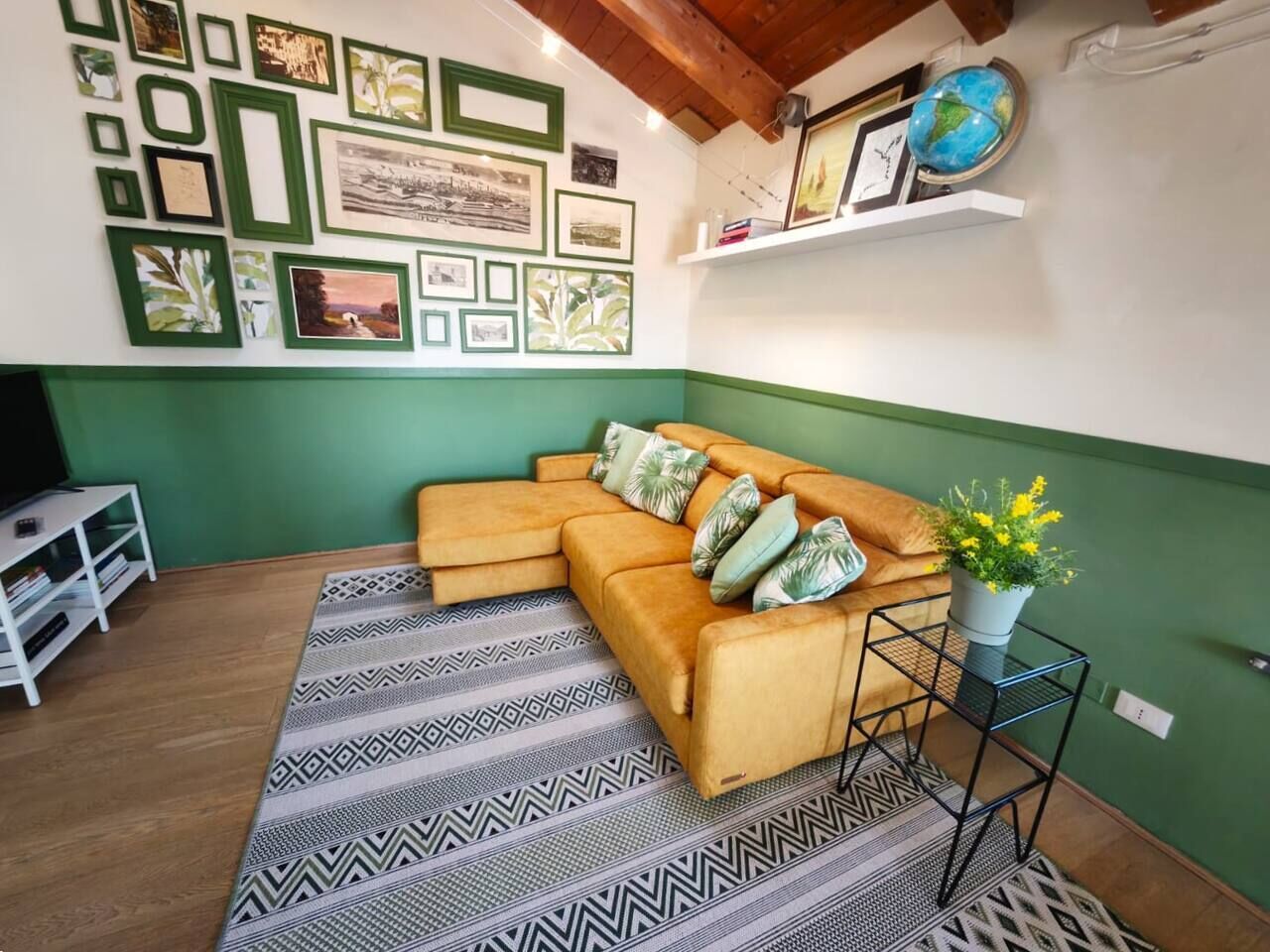 A living room with a sectional sofa, patterned rug, wall art, and a globe on a shelf.
