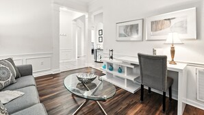 A modern living room with a glass coffee table, a gray sofa, a white desk with a lamp, and framed artwork on the wall. - Huge Lakeview Corner Penthouse WOW (Orlando)