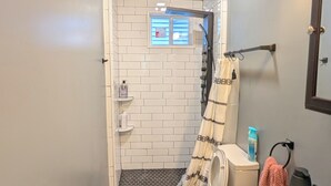 Une petite salle de bain comprenant une douche, des toilettes, un lavabo et une petite fenêtre.