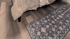 Une chambre à coucher avec un lit, une fenêtre avec des stores, un ventilateur de plafond et un tapis à motifs.