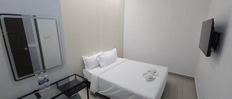 Una habitación pequeña y limpia con una cama, un espejo, un televisor y una mesita de noche con un cubo de basura.