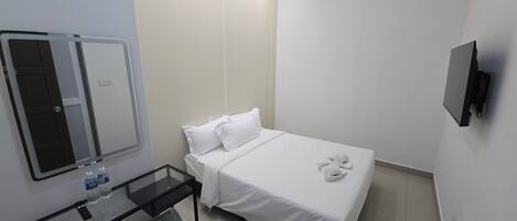 A hotel room with a bed, a bedside table with water bottles, a trash bin, and a TV mounted on the wall.