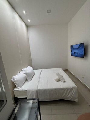 Una habitación de hotel pequeña y moderna con una cama individual, un televisor de pantalla plana en la pared y una mesita.