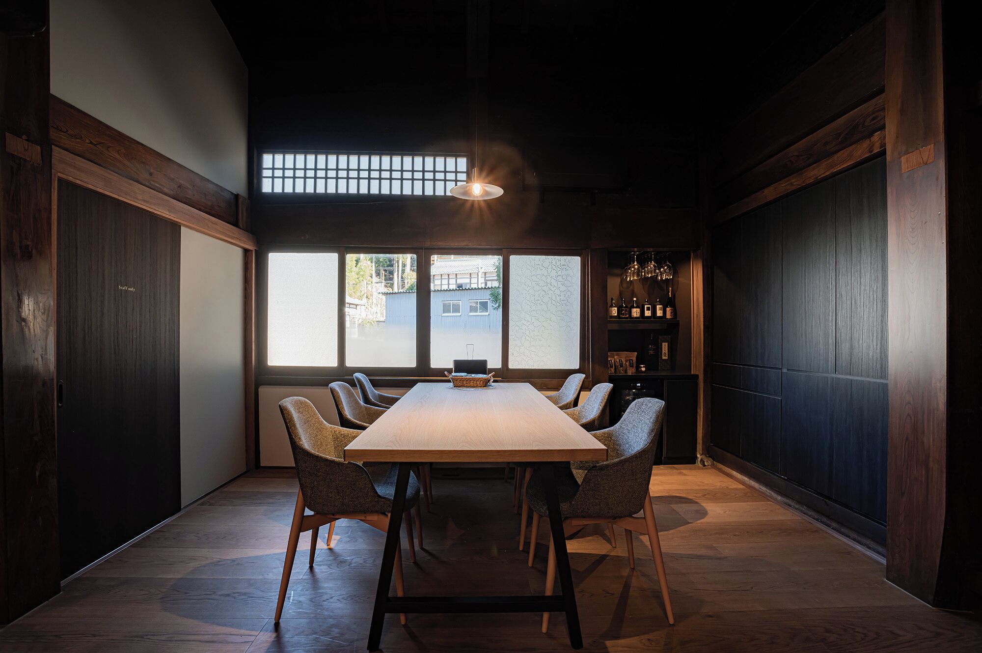 A conference room with a long table, six chairs, and a large window with a view of buildings outside.