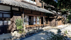 Un edificio japonés tradicional con techo de tejas, estructura de madera y un sendero de grava que conduce a la entrada.