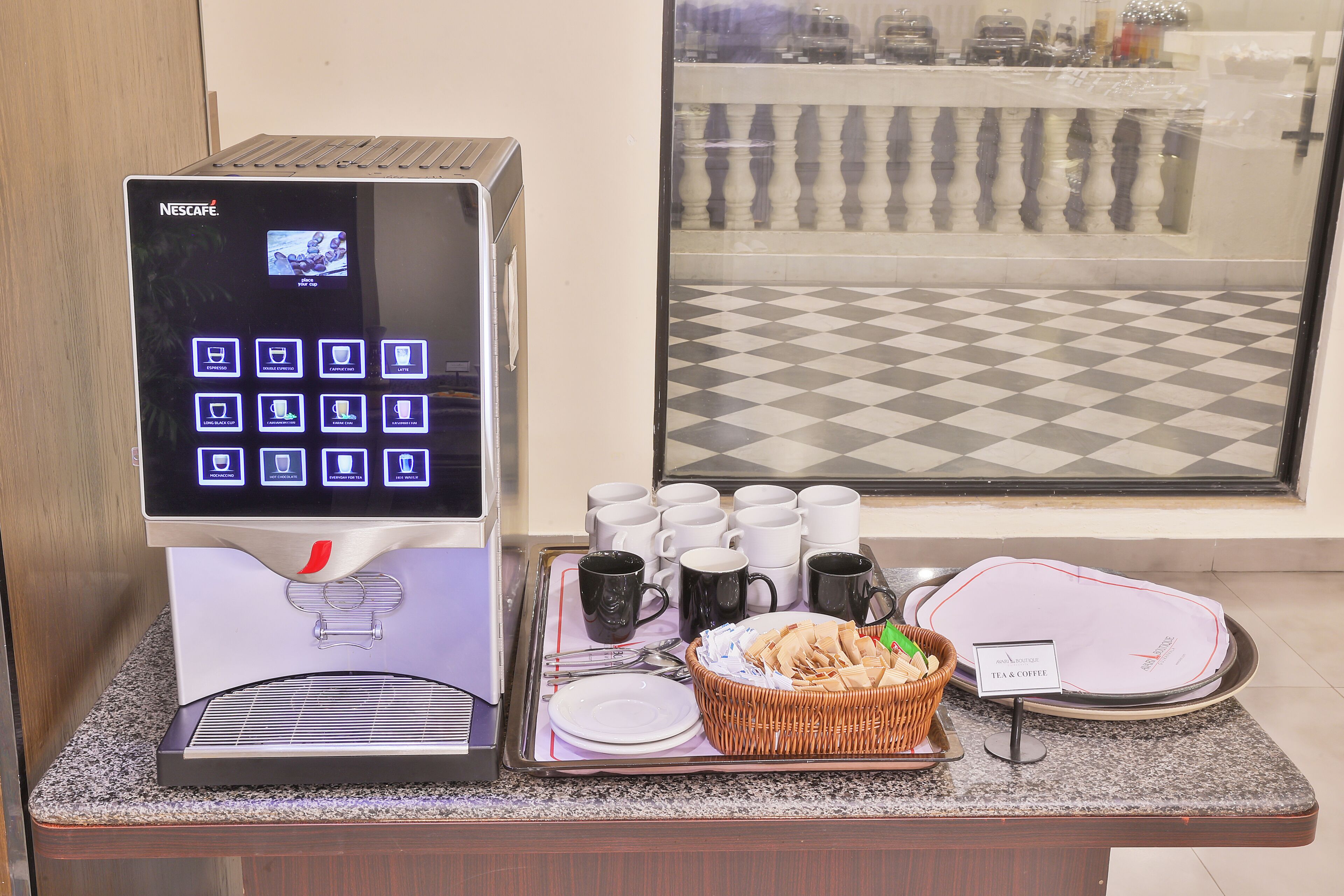 Una máquina de café Nescafé con pantalla digital, una bandeja con tazas, platos y una cesta de pasteles.