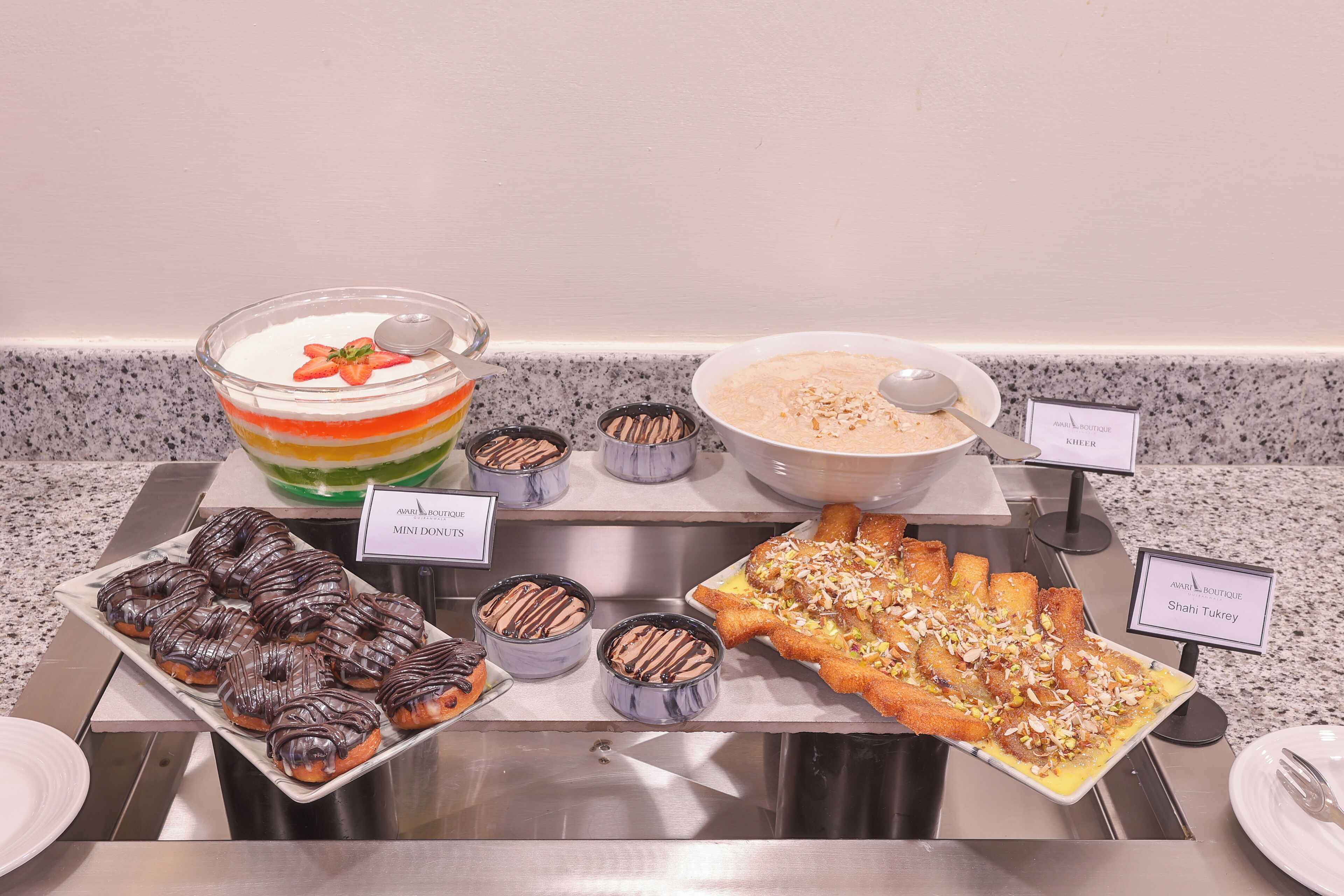 A buffet with various desserts including mini donuts, a layered dessert, and a pastry topped with nuts.