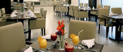 Un comedor de hotel con mesas dispuestas para el desayuno, incluyendo bebidas y un jarrón con flores.