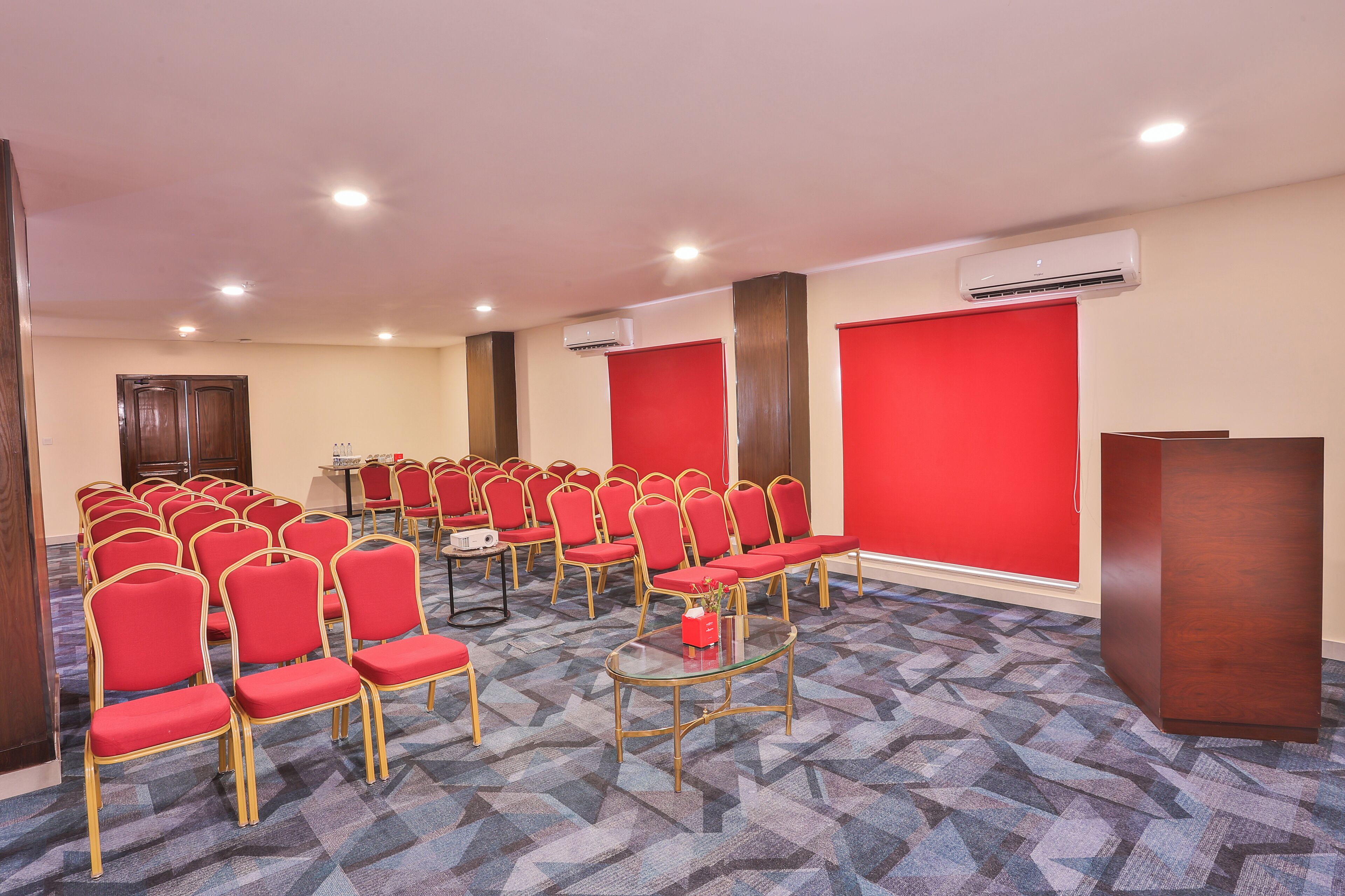 Un salón de conferencias con hileras de sillas rojas, un atril y un equipo de aire acondicionado en la pared.