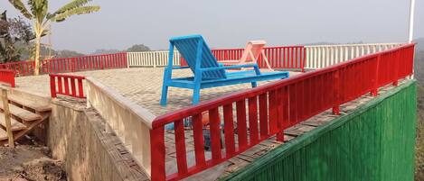 A beach with a wooden staircase leading down to the sand, a red and white railing, and a blue and red lounge chair.