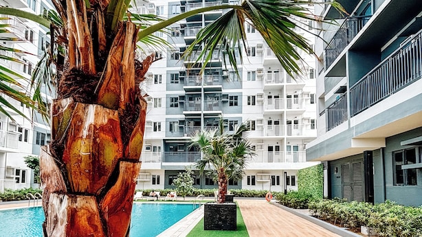 A modern building with a pool, surrounded by palm trees and a well-maintained lawn. - Spacious & Relaxing Haven (Iloilo)