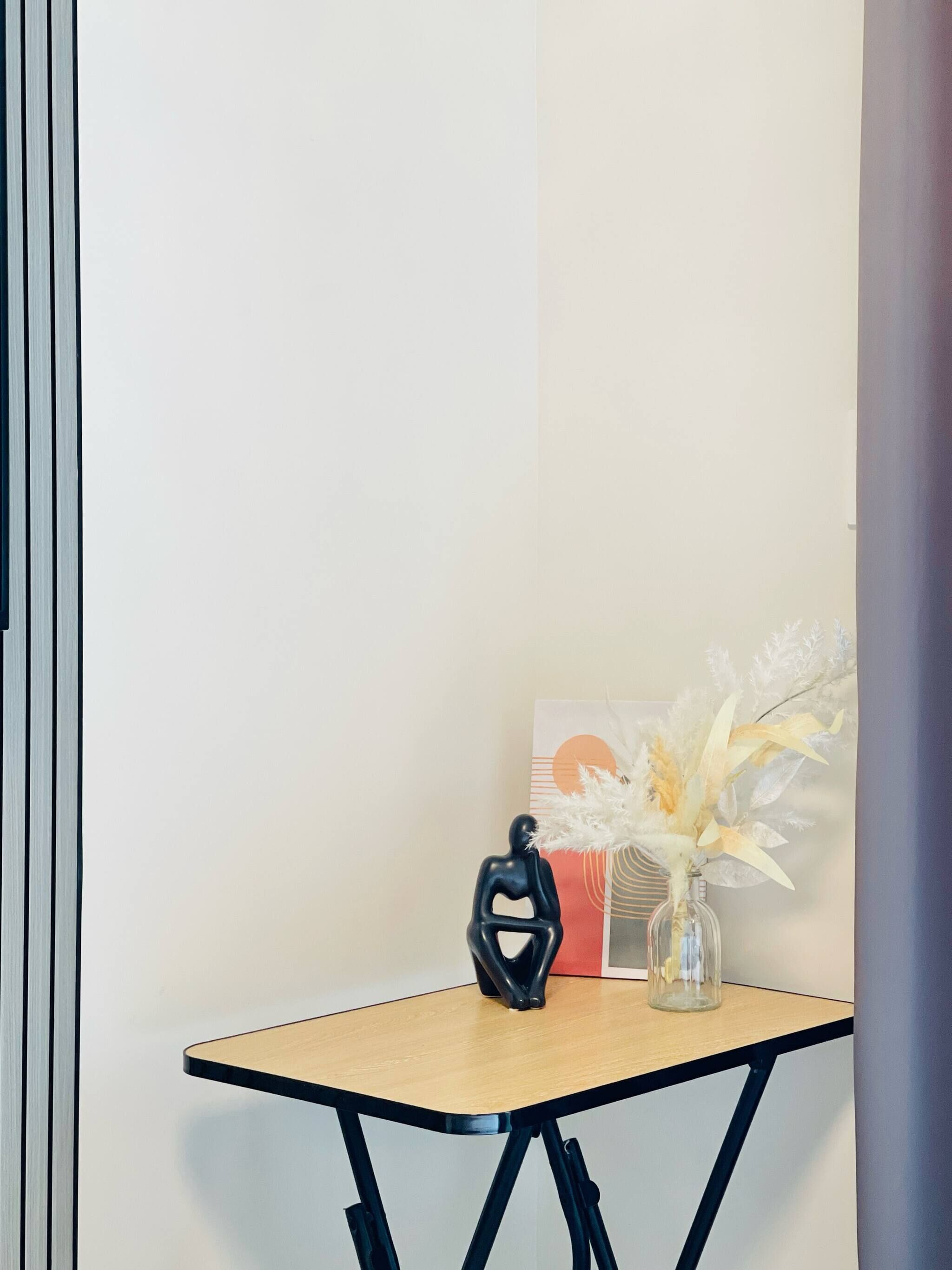 A corner of a room with a small table, a black abstract sculpture, and a vase with white flowers.