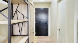 A hallway with a wooden floor, a black door, and a metal-framed shelving unit. - The Perfect Central Getaway (Iloilo)