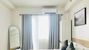 Ett hotellrum med en säng, en spegel, en garderob och ett fönster med gardiner.