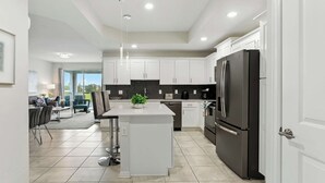 A modern kitchen with white cabinets, a central island, a black refrigerator, and a dining area with a table and chairs. - Beautiful Lakeview Retreat Near Disney (Kissimmee)