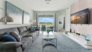A modern living room with a grey sofa, a coffee table, and a TV mounted on the wall. - Beautiful Lakeview Retreat Near Disney (Kissimmee)