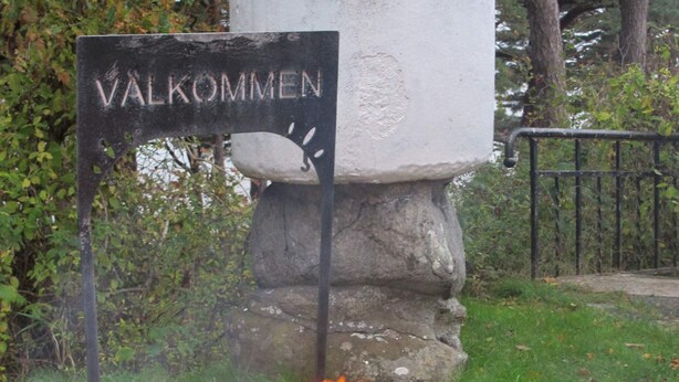 Un cartello con su scritto "VALKOMMEN" fissato a un pilastro di pietra.