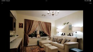 A living room with a sofa, ottoman, and a television. - Charming 2-bedroom apartment in Arverne by the Sea (Arverne)