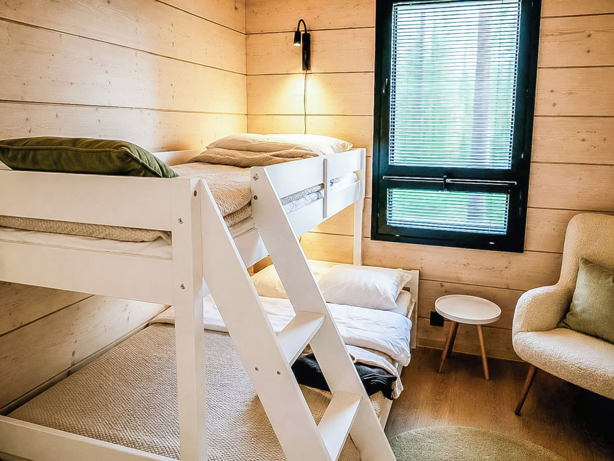 A bunk bed room with a window, a chair, and a small table.