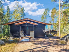 A cabin with a number 66, surrounded by trees, with a gravel path leading to the entrance.