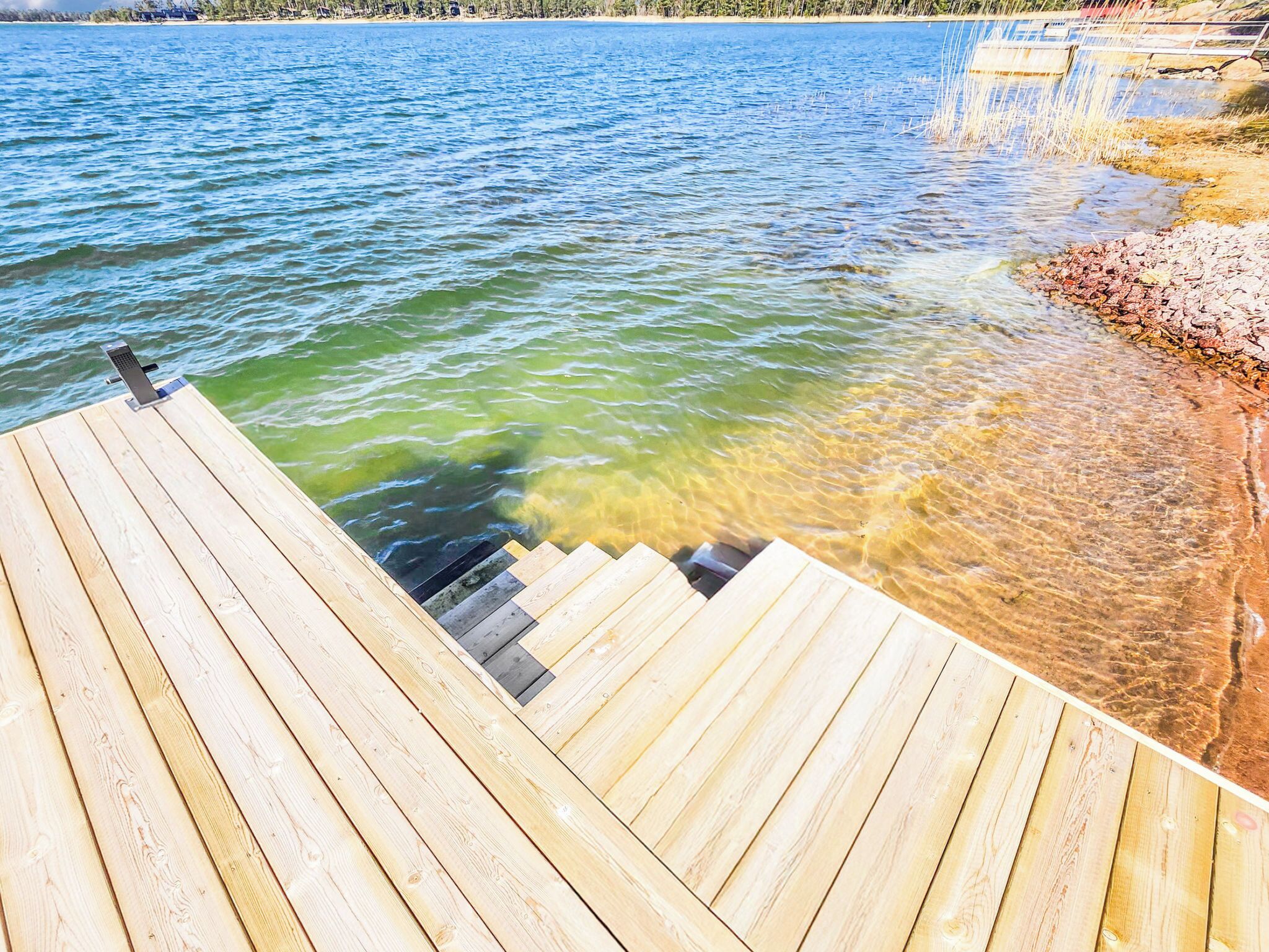 Une jetée en bois s’étendant dans une étendue d’eau, avec des zones peu profondes et claires près du rivage.
