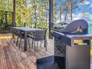 An outdoor patio with a wooden deck, a table with chairs, and a barbecue grill.