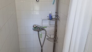 A small, tiled shower stall with a showerhead, a handheld shower, and a metal shelf with toiletries. - Etape Sologne, flexible accommodation (Neuvy-sur-Barangeon)