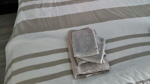 A neatly made bed with striped bedding, two pillows, and a folded towel. - Etape Sologne, flexible accommodation (Neuvy-sur-Barangeon)