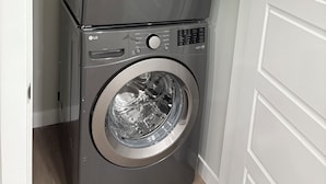 A stacked washer and dryer unit in a laundry room with a white door and light-colored walls. - Cozy, clean and homely (Calgary)