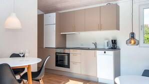 A modern kitchen with wooden cabinets, a built-in oven, and a dishwasher. There is a dining table with chairs and a pendant light above it. - 4 Person Holiday Park Home in Aabenraa (Aabenraa)