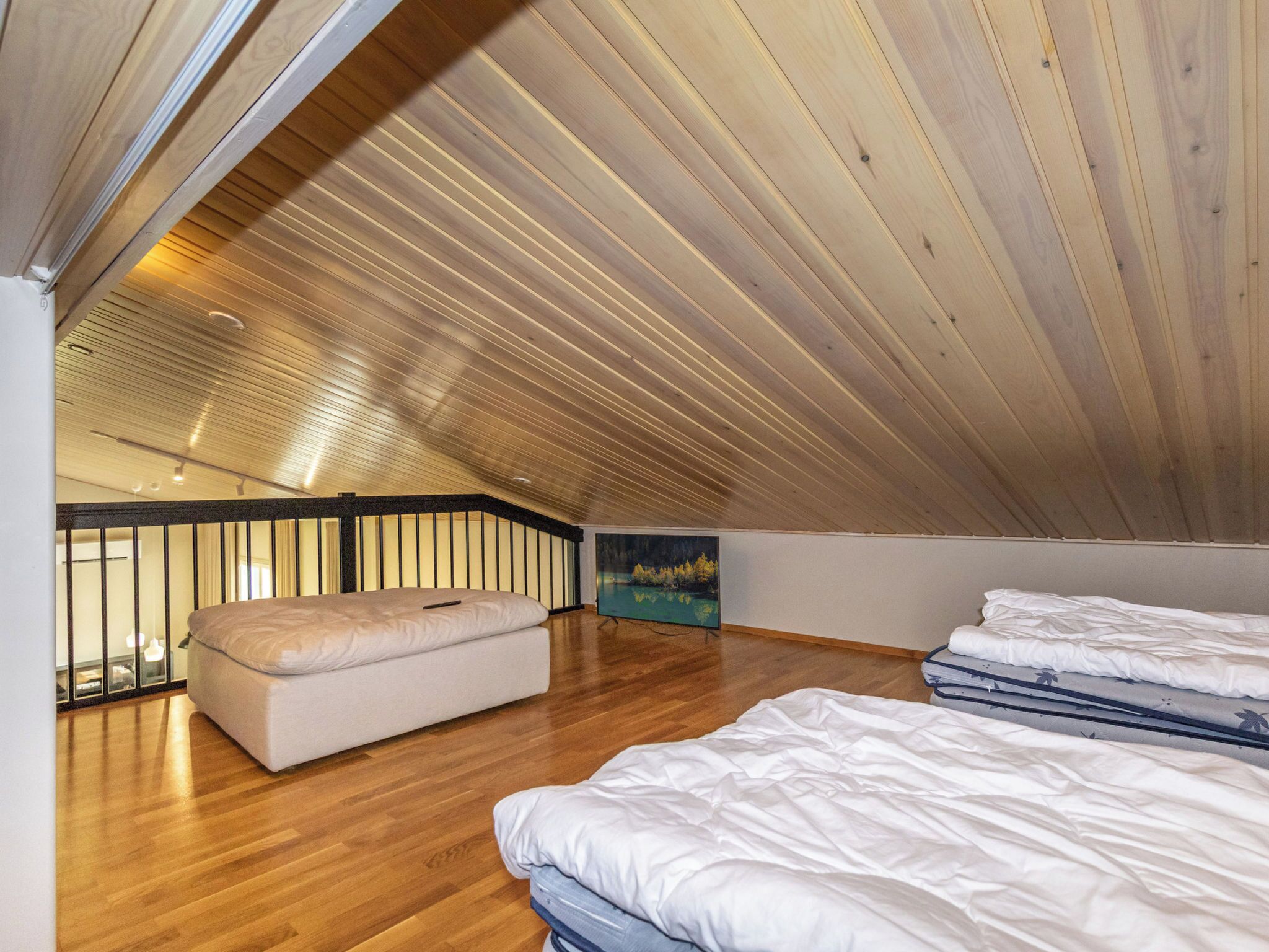 Un dormitorio con techo inclinado, suelo de madera, cama, banqueta y un cuadro.