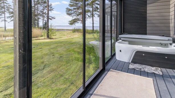 Une terrasse extérieure moderne, dotée d’un jacuzzi, qui offre une vue sur une zone verdoyante et un plan d’eau.