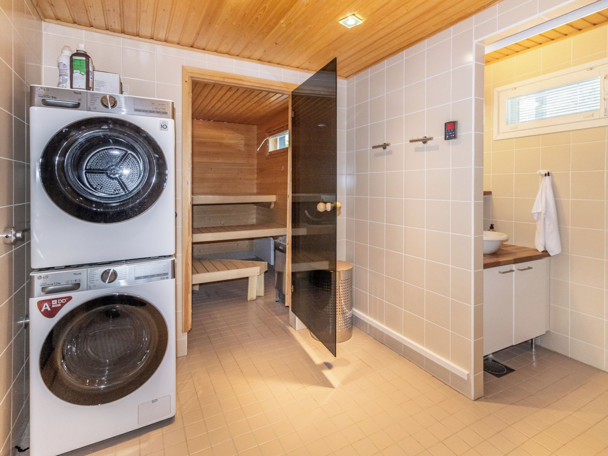 A laundry area with two stacked washing machines, a sauna, and a small bathroom with a sink and towel rack.