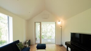 A spacious living room with a black piano, a blue sofa, and a large window providing natural light. - Coboushi Omoya (Niseko)