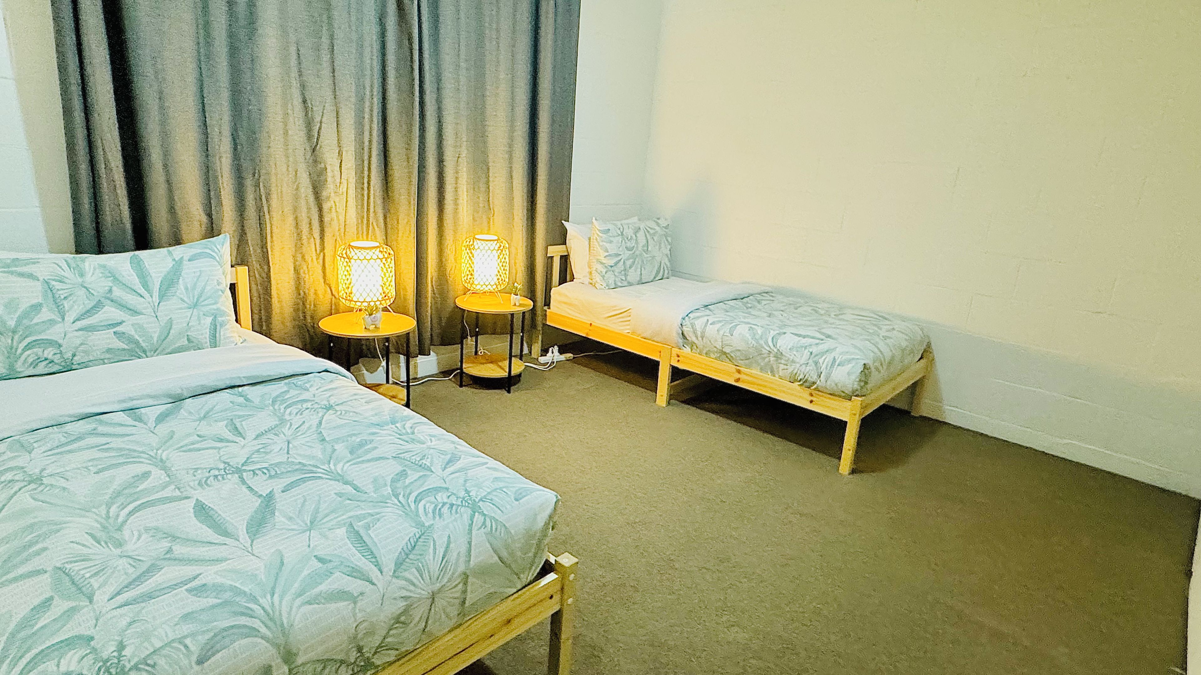Een kamer met twee éénpersoonsbedden, een tafeltje met lampen en een gordijn.