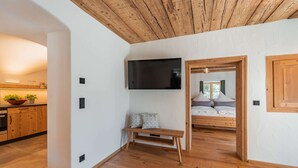 Un interior moderno con techo de madera, televisor de pantalla plana montado en la pared, un banco con cojines y una cama con almohadas.