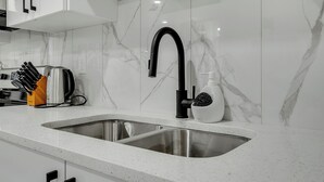 A modern kitchen with white marble backsplash, stainless steel sink, and black faucet. - Serene Luxury Getaway (Calgary)