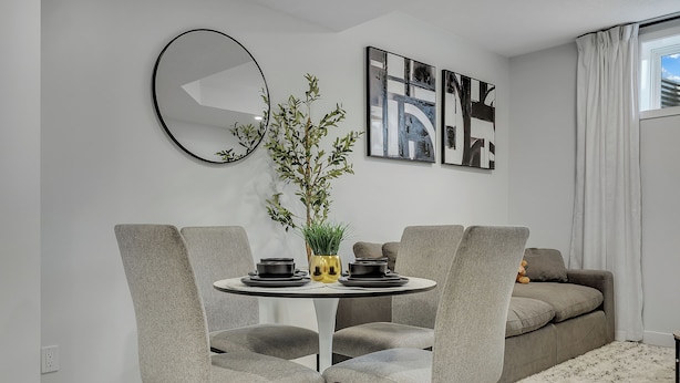 A modern dining area with a round table, grey upholstered chairs, a potted plant, and abstract wall art. - Serene Luxury Getaway (Calgary)