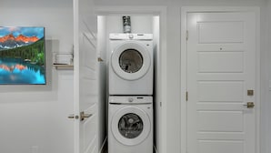 A laundry room with two stacked washing machines, a painting of a mountain lake, and a white door. - Serene Luxury Getaway (Calgary)