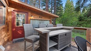 Una cabaña de madera con terraza, una puerta roja, mobiliario de mimbre y vistas al bosque.