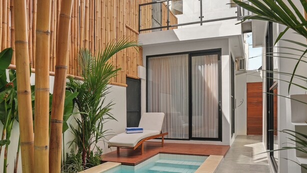 A modern pool area with a bamboo fence, a lounge chair, and a staircase leading to a second-floor balcony.