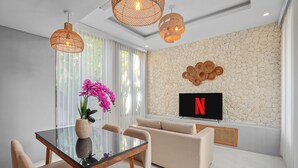 A modern living room with a glass dining table, beige sofa, and a stone wall.